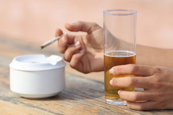 Woman hands holding a cigarette smoking and drinking alcohol in a bar table